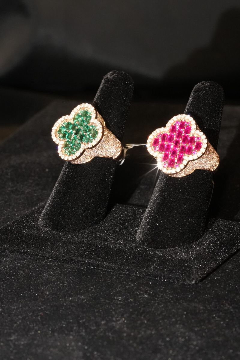 Two clover rings, one emerald and one ruby, on black velvet ring stands